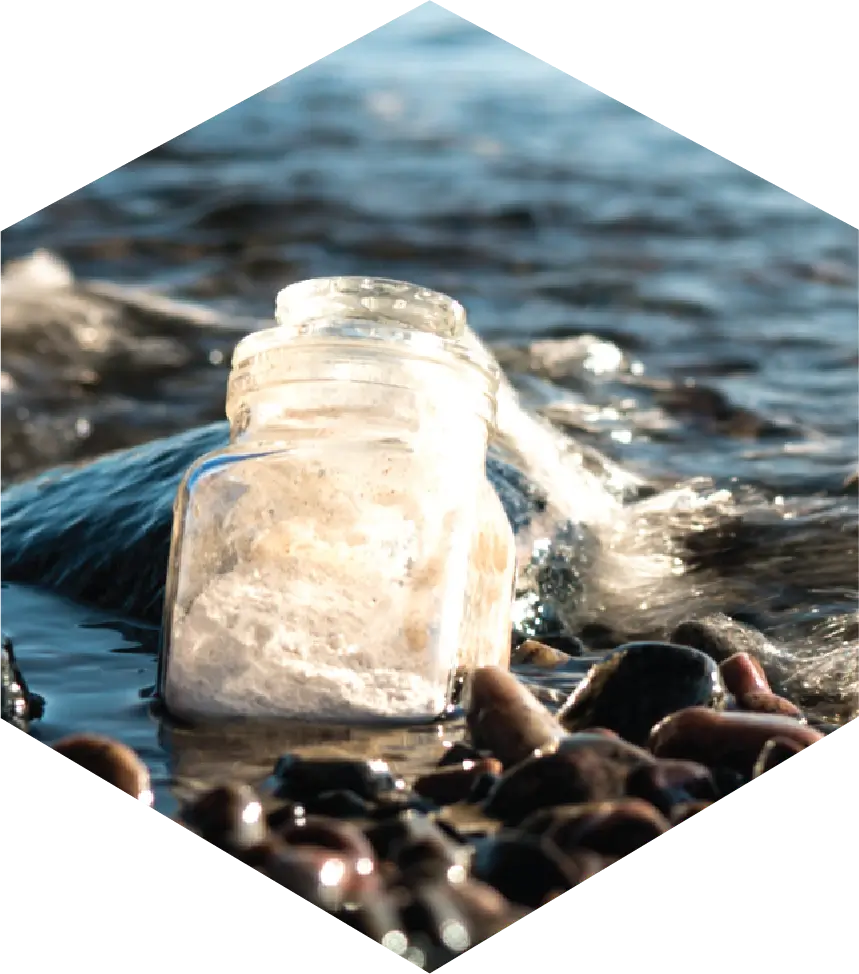 Image of a bottle partially buried in rocky sand in the ocean.