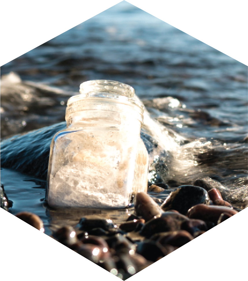 Image of a bottle partially buried in rocky sand in the ocean.